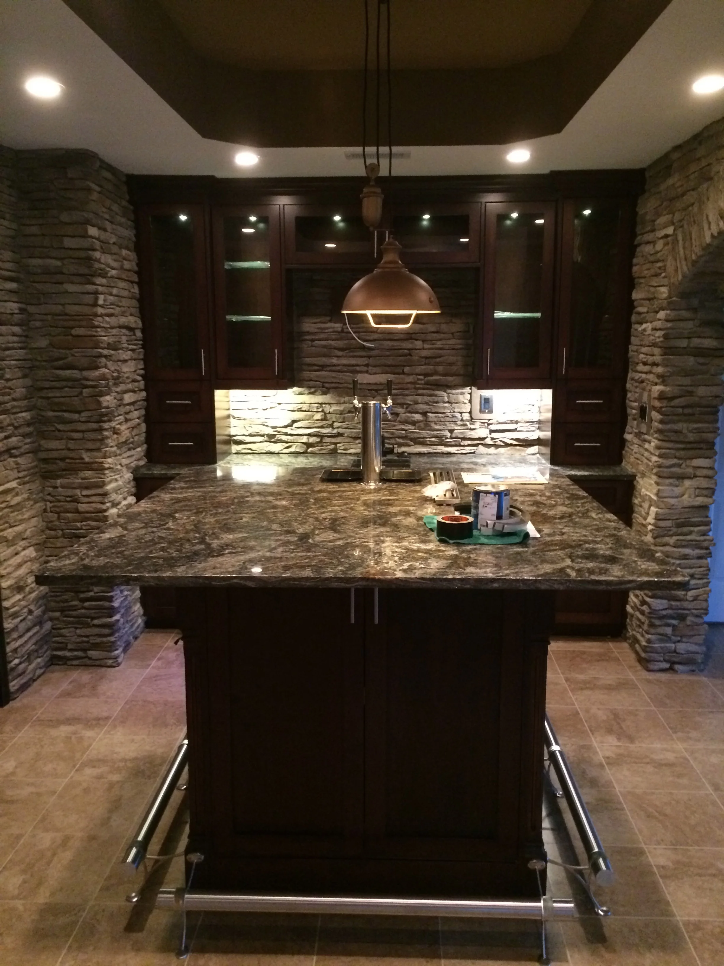 Modern kitchen with stacked stone walls, dark cabinets, granite counters, and pendant lighting