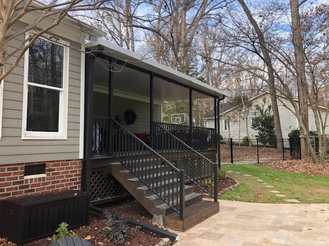 Black-framed screened porch with glass panels, composite deck, and metal railing attached to brick home