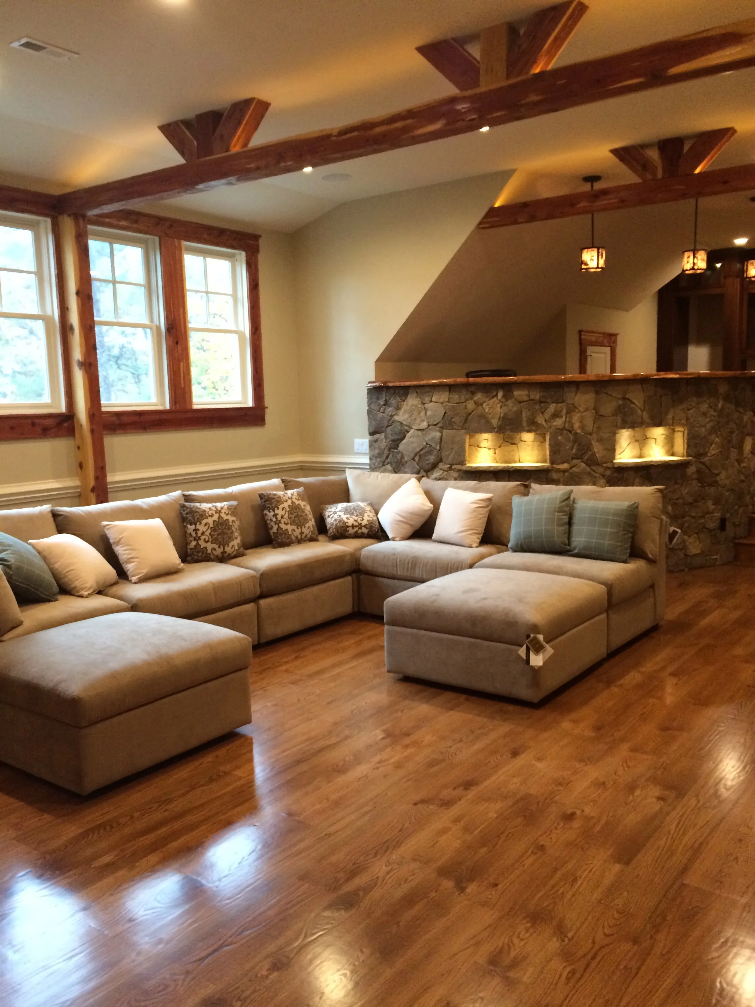Finished basement with wood beams, stone fireplace, hardwood floors, and sectional seating
